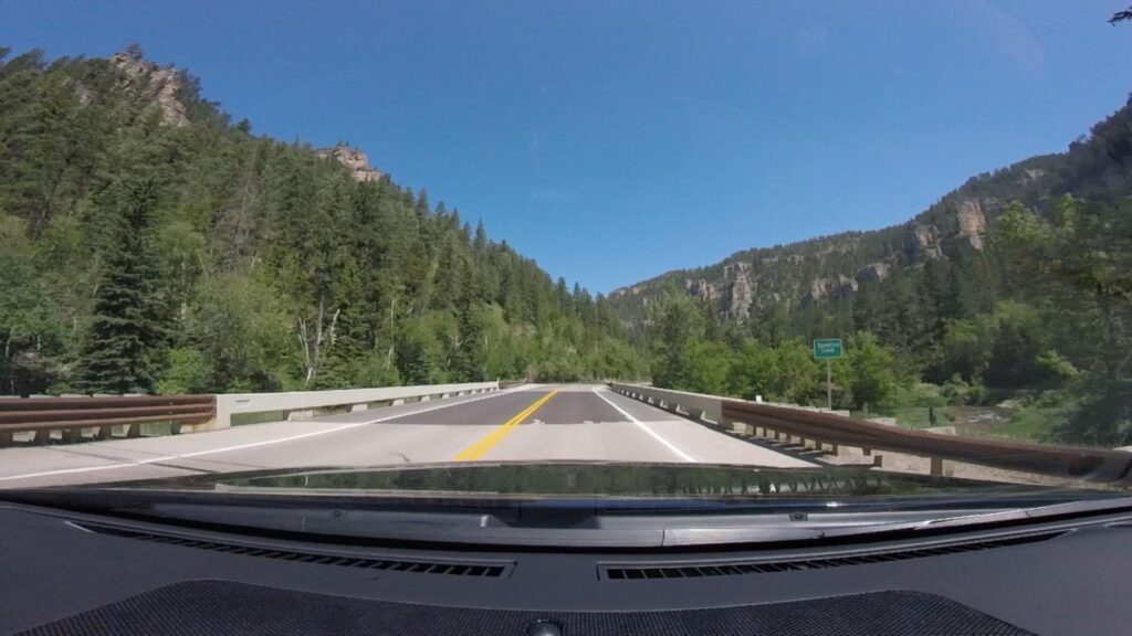 A car driving down a mountain road through Spearfish Canyon Scenic Byway with mountains in the background.